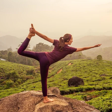 Woman in a yoga pose on a rock overlooking green hills
